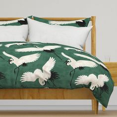 a bed with green and white bedspread that has cranes on it, along with two pillows