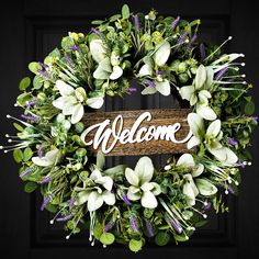 a wreath with the word welcome written on it and flowers around it in front of a black door