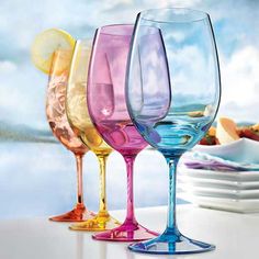 four different colored wine glasses sitting on a table with plates and bowls in the background