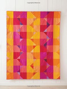 an orange and pink quilt hanging on the wall