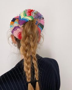 a woman with long hair wearing a multicolored headband and braid in front of a white wall