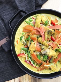 a skillet filled with vegetables on top of a wooden table next to a knife