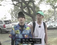 two young men standing next to each other in front of a tree and some cars