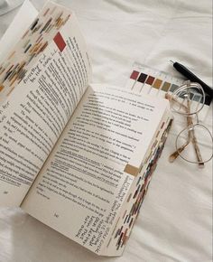 an open book sitting on top of a bed next to reading glasses and eyeglasses