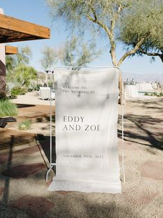 a white towel hanging from a clothes rack in front of a building with trees and bushes