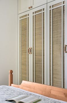 an open book sitting on top of a bed next to a white cupboard and window