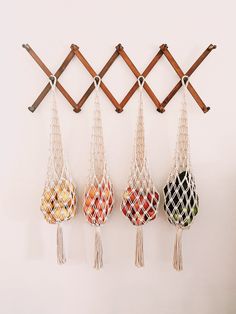 four macrame bags hanging on a wall with wooden pegs and string attached to them