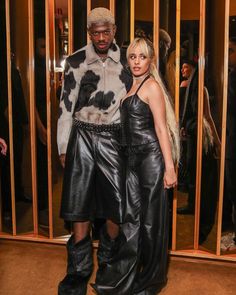 a man and woman standing next to each other in front of a glass door wearing black leather pants