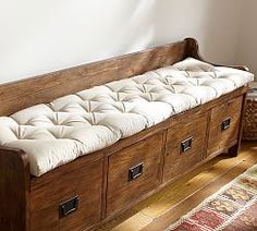 a wooden bench with white cushions on it in a living room next to a rug