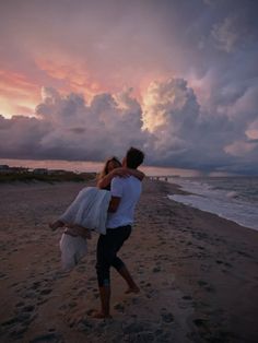 a man and woman hug on the beach at sunset