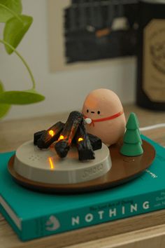 an egg sitting on top of a book next to a small christmas tree and fire