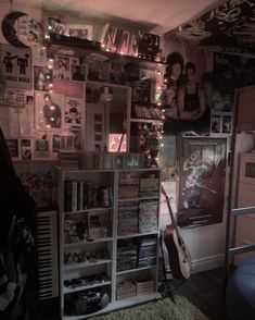 a room filled with lots of musical equipment and pictures on the wall above it is a guitar propped up against a bookcase