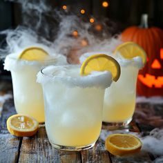 two glasses filled with ice and lemons on top of a wooden table next to pumpkins