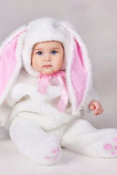 a baby wearing a bunny suit and pink bow tie sitting in front of a gray background