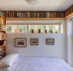 there is a bed in the room with books on the shelves above it and two windows