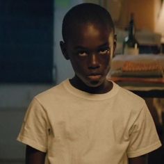 a young boy in a white t - shirt is staring at the camera