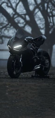 a black motorcycle parked on top of a dirt field next to a tree in the fog