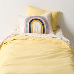 a yellow comforter with a rainbow pillow on the bottom and white bedding underneath