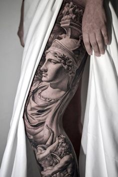 a man's leg with tattoos on it and an image of a statue in the background