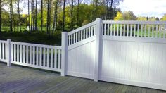 a wooden deck with a white fence and gated in area next to the woods