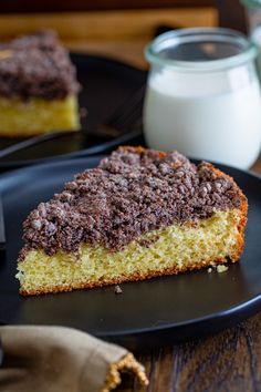 a piece of cake sitting on top of a black plate next to a glass of milk