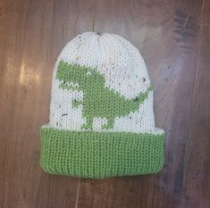 a green and white knitted beanie with an image of a dinosaur on it