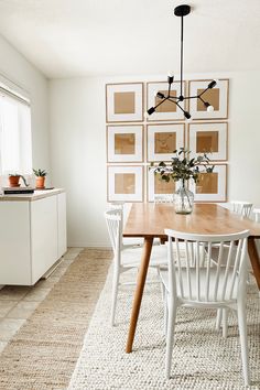 a dining room table and chairs with pictures on the wall behind it in front of a window