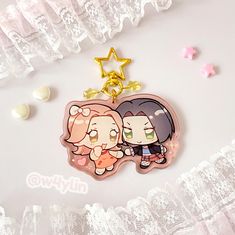 two cartoon characters are hanging from a keychain on a white surface with stars and confetti around them