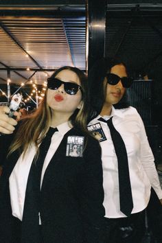 two people dressed in black and white posing for the camera with their cell phones up to their ears