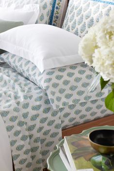 a vase with white flowers sitting on top of a bed next to pillows and blankets