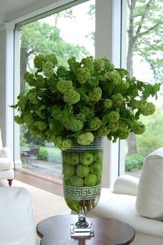 a vase filled with green apples sitting on top of a table next to a window