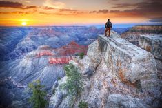 a man standing on the edge of a cliff looking out at the grand canyon as the sun sets