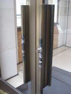 an open glass door in front of a white tiled floor and wall with two handles on each side