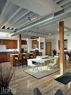 an open concept living and dining area with wood flooring, white chairs, stainless steel appliances and large windows