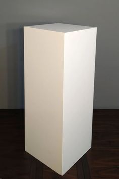 a white square object sitting on top of a wooden floor next to a gray wall