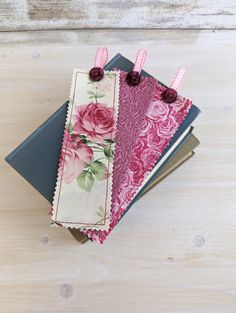 three notebooks with pink flowers on them sitting on top of each other next to a wooden table