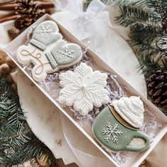 decorated cookies in a box on a table with pine cones and other christmas decorating items