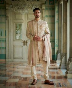 a man standing in front of a doorway wearing a white and beige sherve