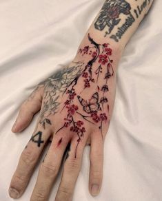 a person with tattoos on their arm and hand is holding onto a white sheet that has red flowers on it