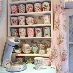 a shelf filled with cups and saucers next to a wall mounted teapots