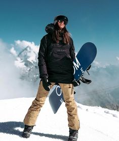 a woman holding a snowboard on top of a mountain