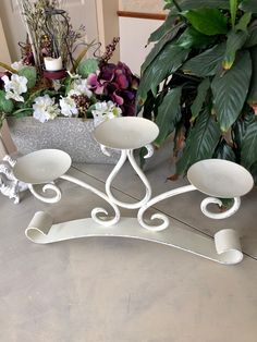 a white candle holder sitting on top of a table next to potted plants and flowers