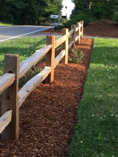 a wooden fence sitting on the side of a road next to a lush green field