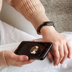 a person holding a cell phone in their left hand while sitting on a couch with white pillows