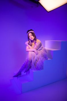 a woman sitting on top of a set of stairs in front of a purple background