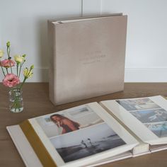 an open book sitting on top of a wooden table next to a vase with flowers