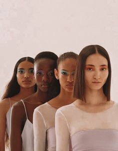 four models with different colored makeup on their faces and body, standing in front of a white background