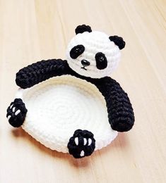 a small crocheted panda bear sitting on top of a white plate with black paws