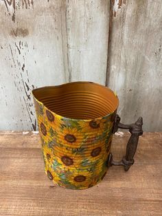 a yellow sunflower print bucket with handles on a wooden table next to a wall