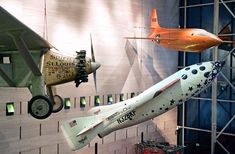 an airplane and rocket are on display in a museum room with other objects hanging from the ceiling